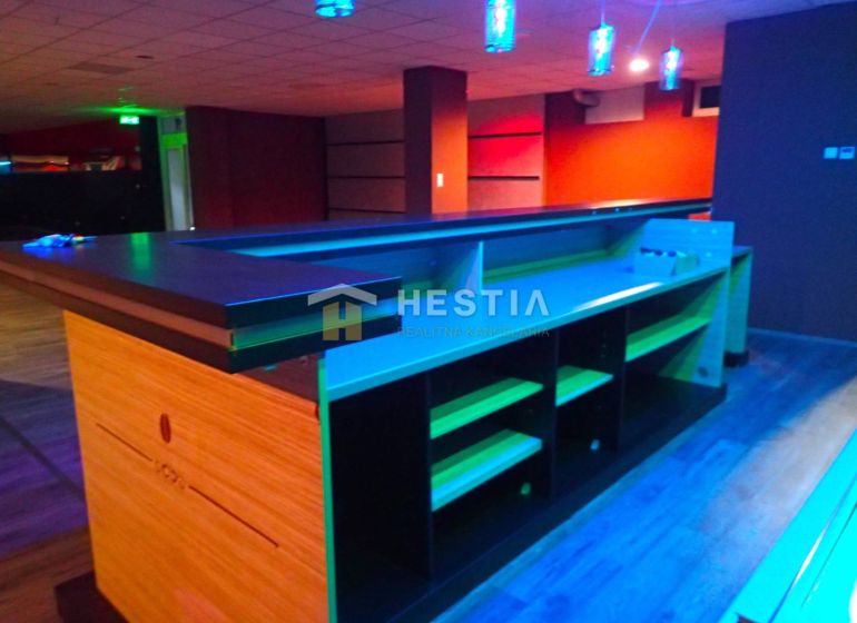 A bar counter in commercial premises with ceiling lighting, wooden and colorful flooring.