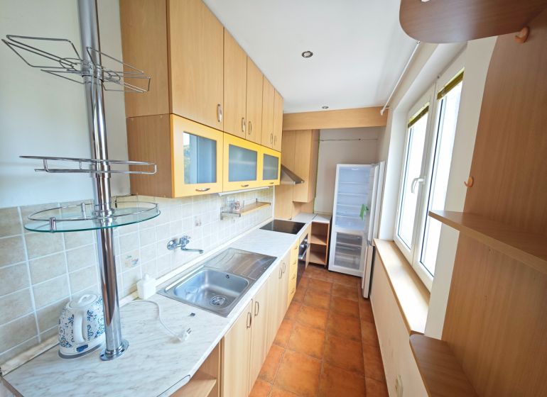 A kitchen in a 3-room apartment with a cooktop, cabinets, and windows, and a floor with a wooden decor.