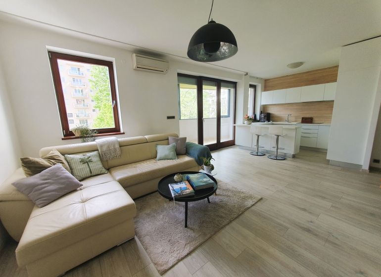 Living room with a kitchenette, sofa, and wooden decor flooring in a 3-room apartment.