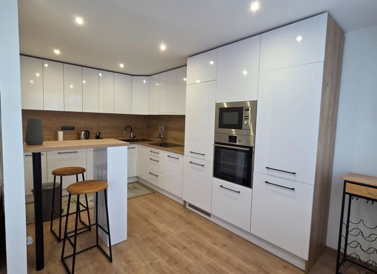 A kitchen in a 3-room apartment with bar seating and a floor with a wooden decor.