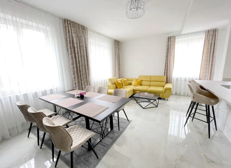 A bright living room with a dining table, a yellow sofa, and bar stools in a three-room apartment.