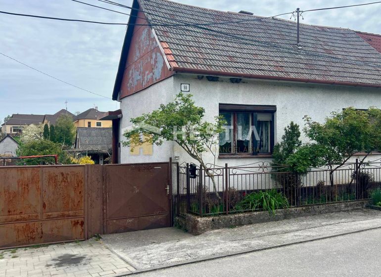 A family house in Cerová with a gate and a small garden, surrounded by greenery.