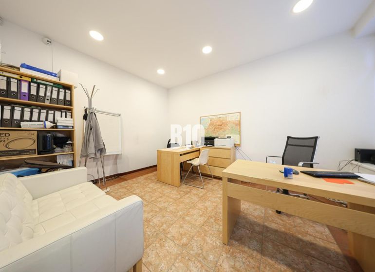 An office with wooden desks, a shelf with documents, a white chair, and a map on the wall.