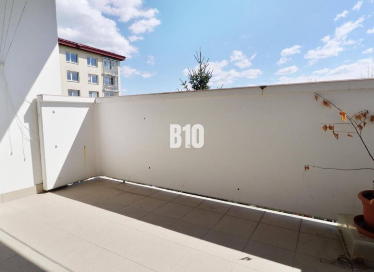 Balcony in a 3-room apartment. Plant in a pot, tiles, partial view of the neighboring building.