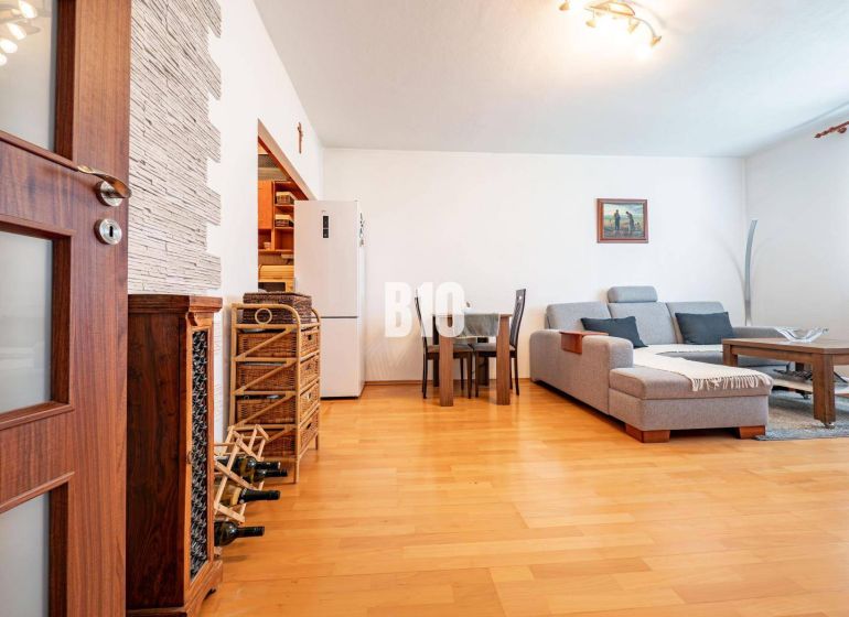 Living room in a two-room apartment with a wooden decor floor, a sofa, and a dining table.