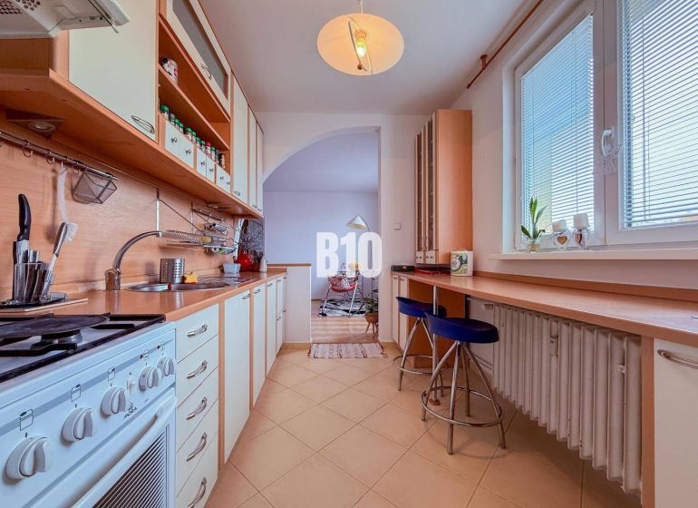 A kitchen in a 3-room apartment with a long work counter and a gas stove.