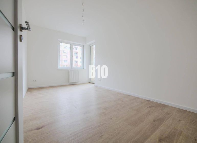 A room with a wooden decor floor in a 3-room apartment and large windows.
