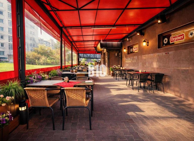 An outdoor terrace of a building in Čadca with tables, a red roof, and greenery.