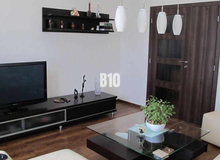 Living room with a television, shelves, a table, and a wooden decor floor in a 4-room apartment.
