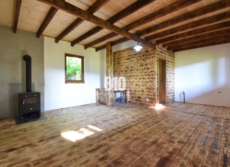 Interior of a cabin with wooden beams and a fireplace, wooden floor and white walls.