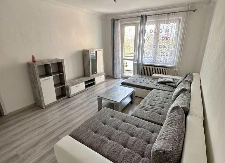 Living room in a 3-room apartment with a wooden decor floor, a large sofa, and a television.