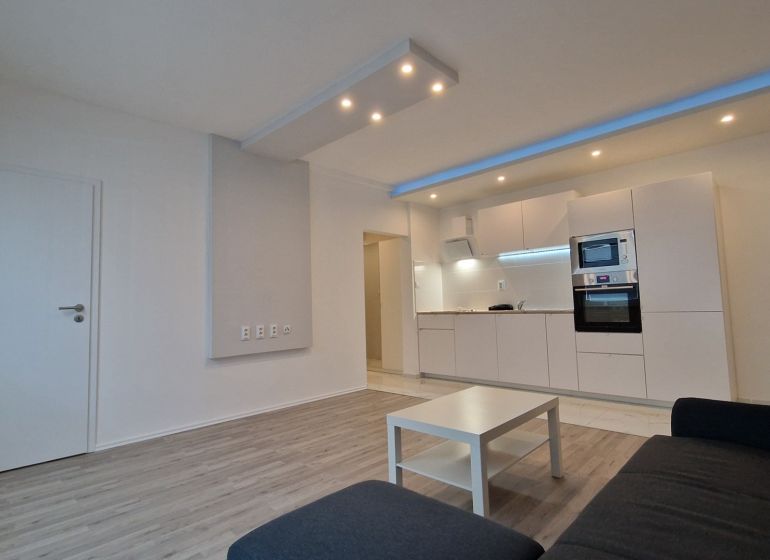 Living room with kitchen in a 2-room apartment, white furniture set, wooden decor flooring.