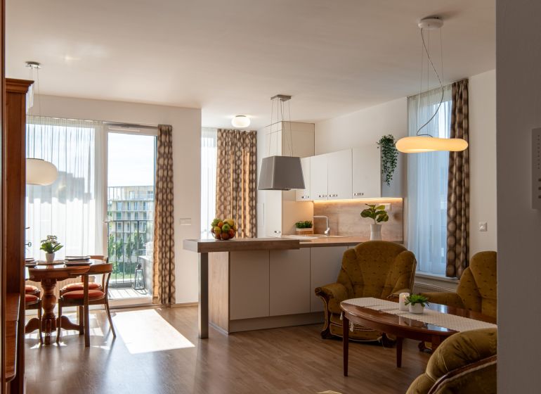 Living room in a two-room apartment with a wooden decor floor and a light kitchen.