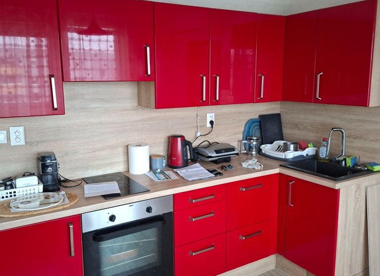 A kitchen in a 2-room apartment with red cabinets and a wooden decor floor.