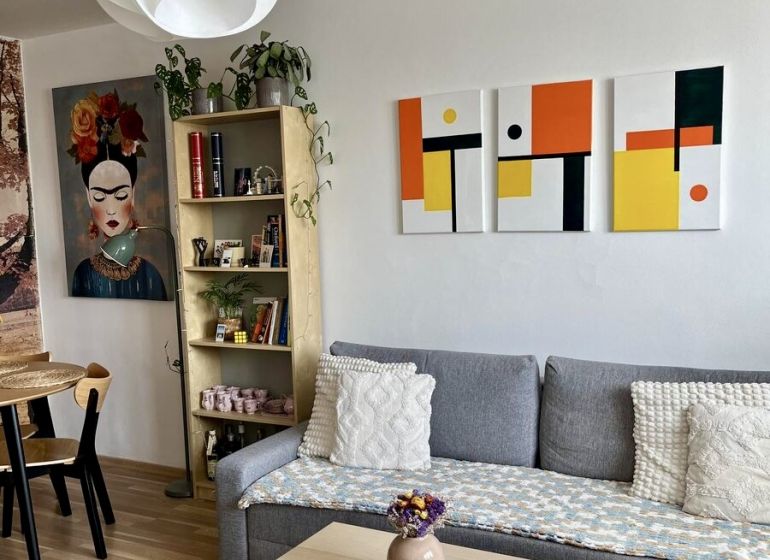 Living room in a two-room apartment with a sofa, table, and wooden decor flooring.