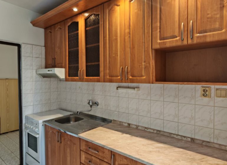 A kitchen in a 2-room apartment with a wooden decor kitchen unit and white tiles.