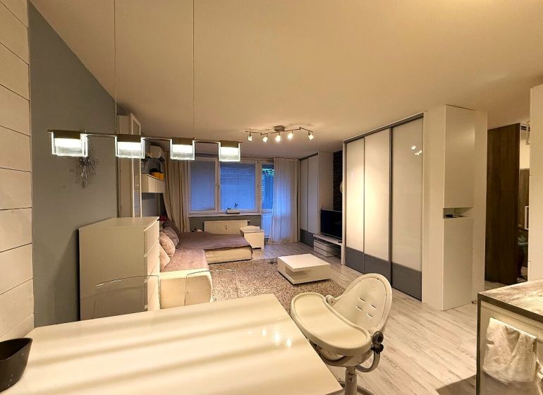 Interior of a 2-room apartment with a wooden decor floor, a large sofa, and a dining table.
