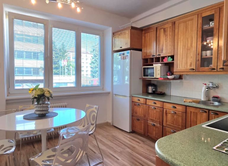 A kitchen in a 2-room apartment with a light table, wooden cabinets, and a floor with a wooden decor.