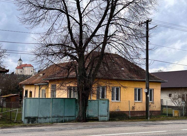 A family house in Komjatice with an orange facade, in front of which there is a large tree.
