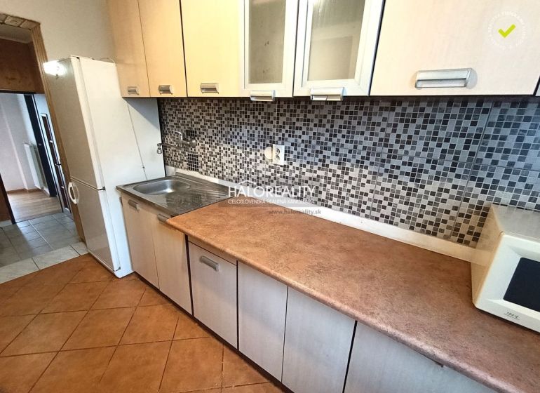 A kitchen of a three-room apartment with mosaic tiles and a wooden decor floor.