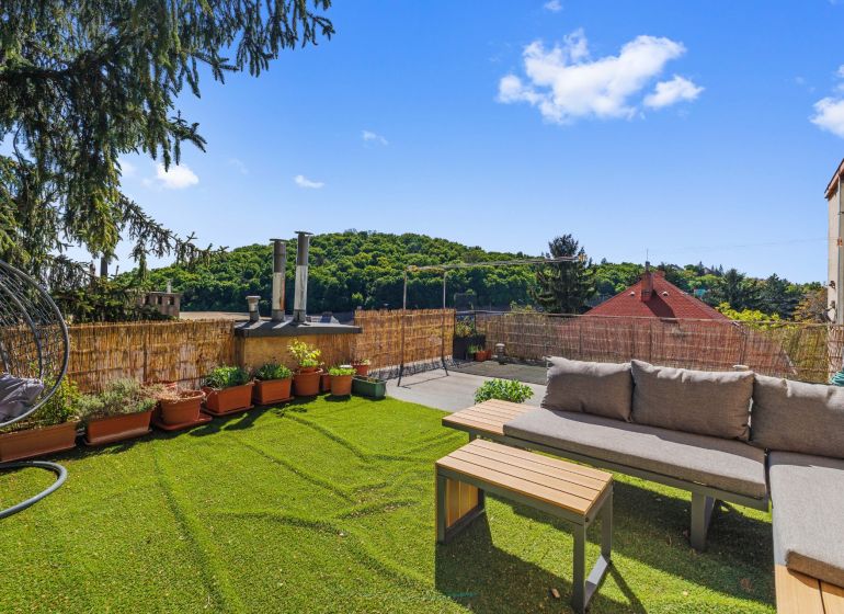 Terrace with a view of greenery, sofa, swing, and potted plants.