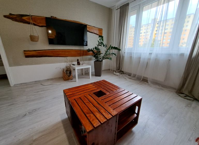 Living room in a 3-room apartment with a television, wooden table, and white curtains.