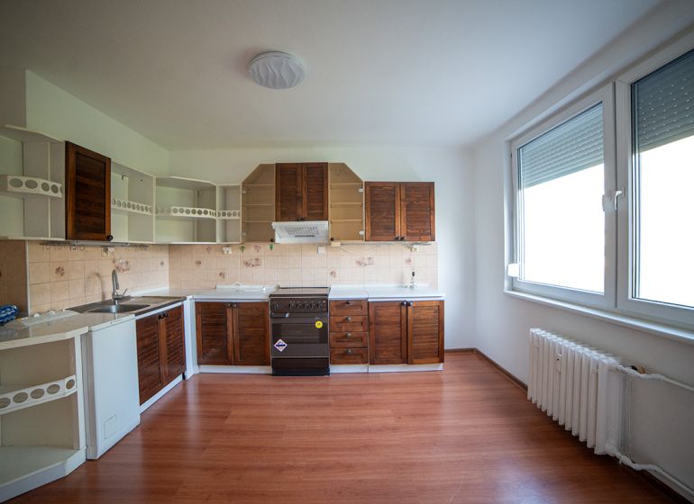 A kitchen in a 2-room apartment with a wooden decor floor and wooden cabinets.