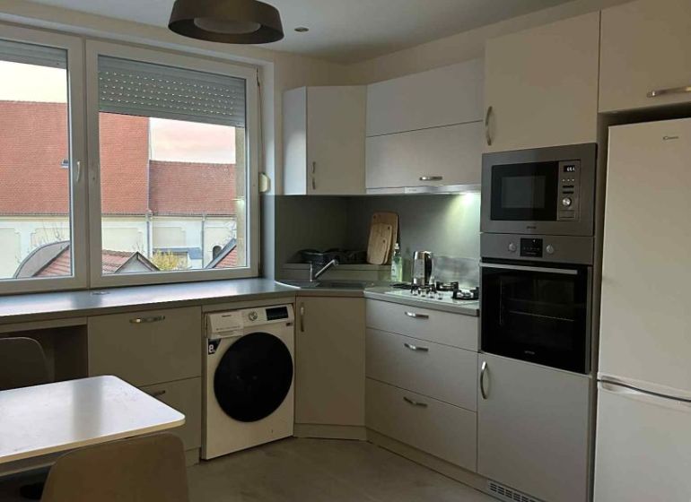 A kitchen with a dining table, built-in appliances, and a wooden decor floor in a studio apartment.