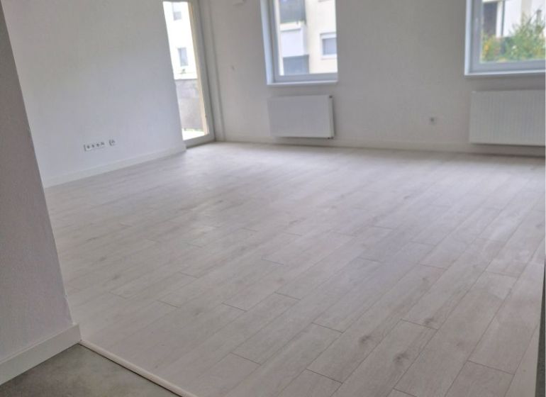 A spacious room in a 3-room apartment with a wooden decor floor and large windows.