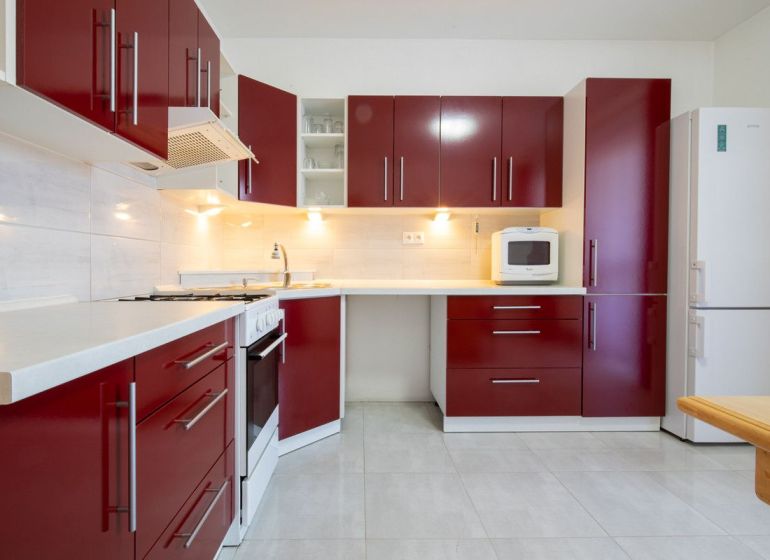 A kitchen with red cabinets in a family house, white appliances, light tiles.