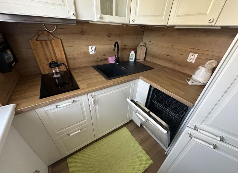 A kitchen in a studio apartment with a wooden decor countertop, built-in dishwasher, and sink.