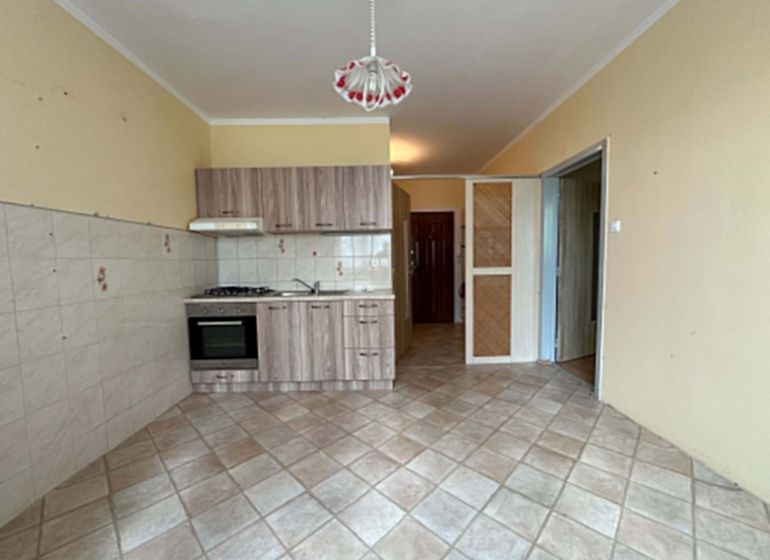 A kitchen in a studio apartment with a tiled floor and light-colored furniture.