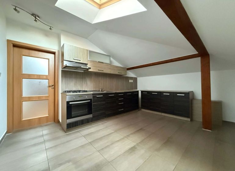 A kitchen in the attic of a 3-room apartment with dark cabinets and a skylight.