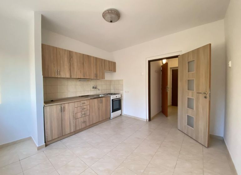 A kitchen in a studio apartment with tiled flooring and wooden decor cabinets.
