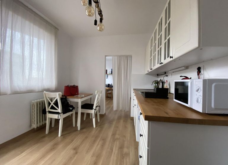 White kitchen with wood-patterned flooring, table, and chairs in a studio apartment.