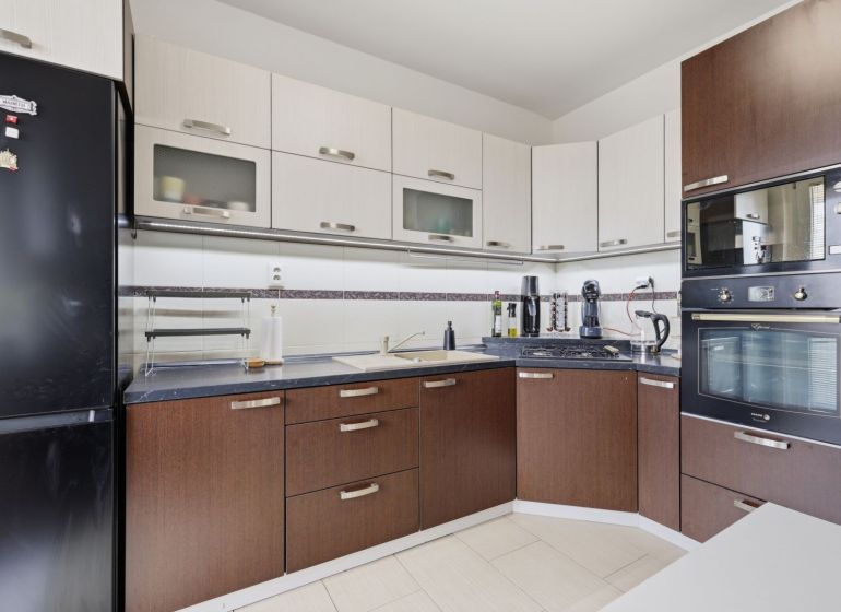 A kitchen in a 3-room apartment with dark furniture and built-in appliances.