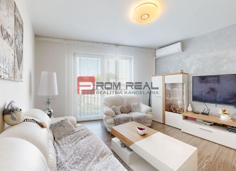 Living room in a two-room apartment with a wooden decor floor, a comfortable sofa, and a television.