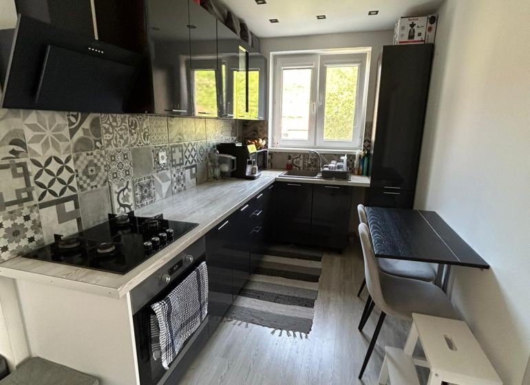 A kitchen with mosaic tiles and a wooden decor floor in a 3-room apartment.