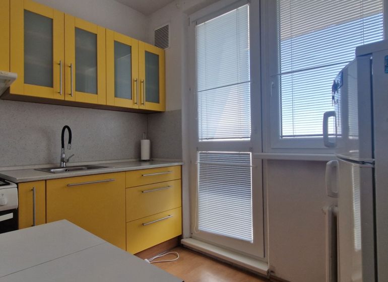 A kitchen with yellow cabinets in a 2-room apartment, floor with wood decor.