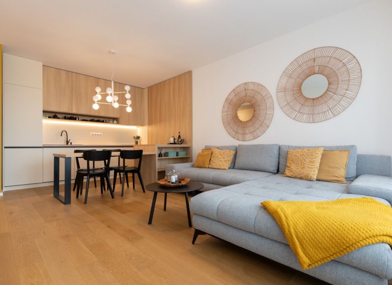 Living room with a kitchen in a 2-room apartment, wooden decor flooring, light-colored sofa.
