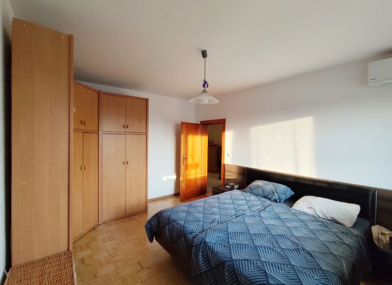 Bedroom in a two-room apartment with a bed, wardrobe, and wooden decor flooring.