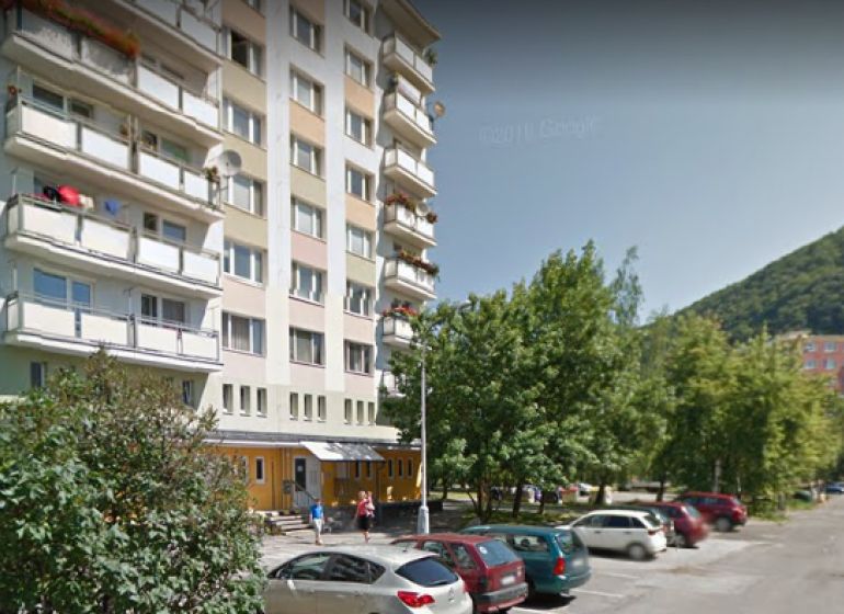 Banská Bystrica: Apartment building with 1-bedroom apartments, greenery, and contact information for the real estate agency.