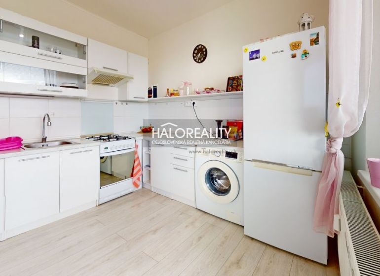A kitchen in a 2-room apartment with white cabinets and a washing machine. Floor with wood decor.