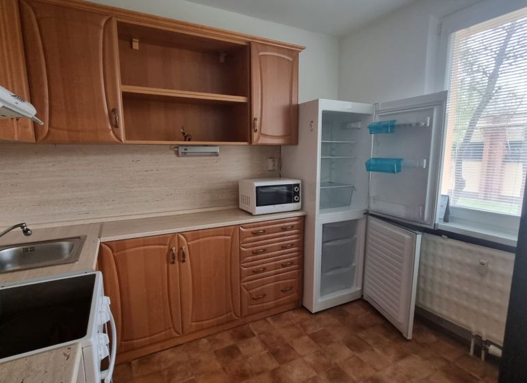 A kitchen in a studio apartment with wooden cabinets, a microwave, and an open refrigerator.