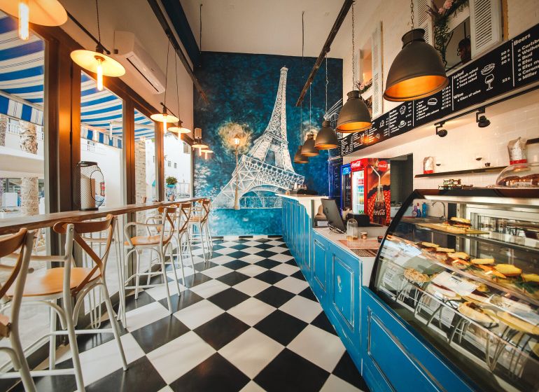 A café with a black and white floor, the Eiffel Tower on the wall, bright lights, wooden chairs.