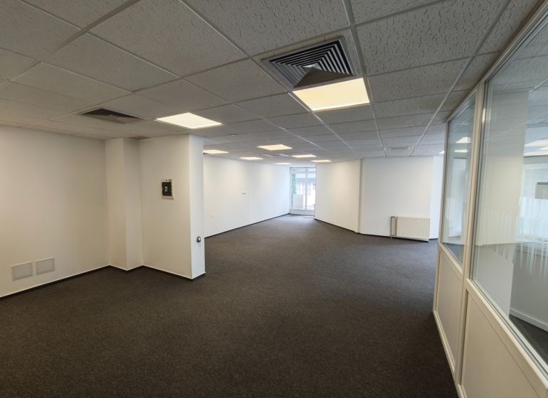 Offices with carpet, white walls, suspended ceiling, partitions with glass, elongated space.
