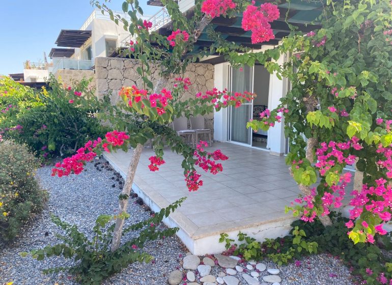 The floral exterior of a 2-bedroom apartment in Tatlisu with a terrace and a garden path.
