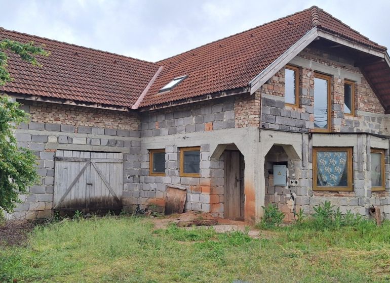 A family house in Stará Bašta made of gray brick with a red roof and wooden doors.