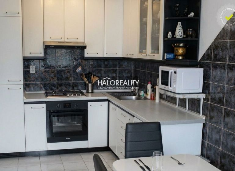 A kitchen unit with white cabinets and dark tiled backsplash in a 3-room apartment.