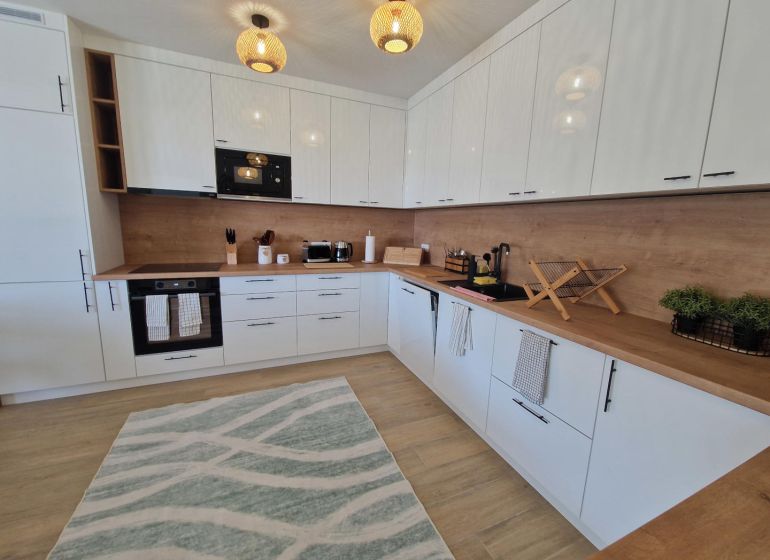A modern kitchen in a 3-room apartment with light furniture and a wooden decor floor.